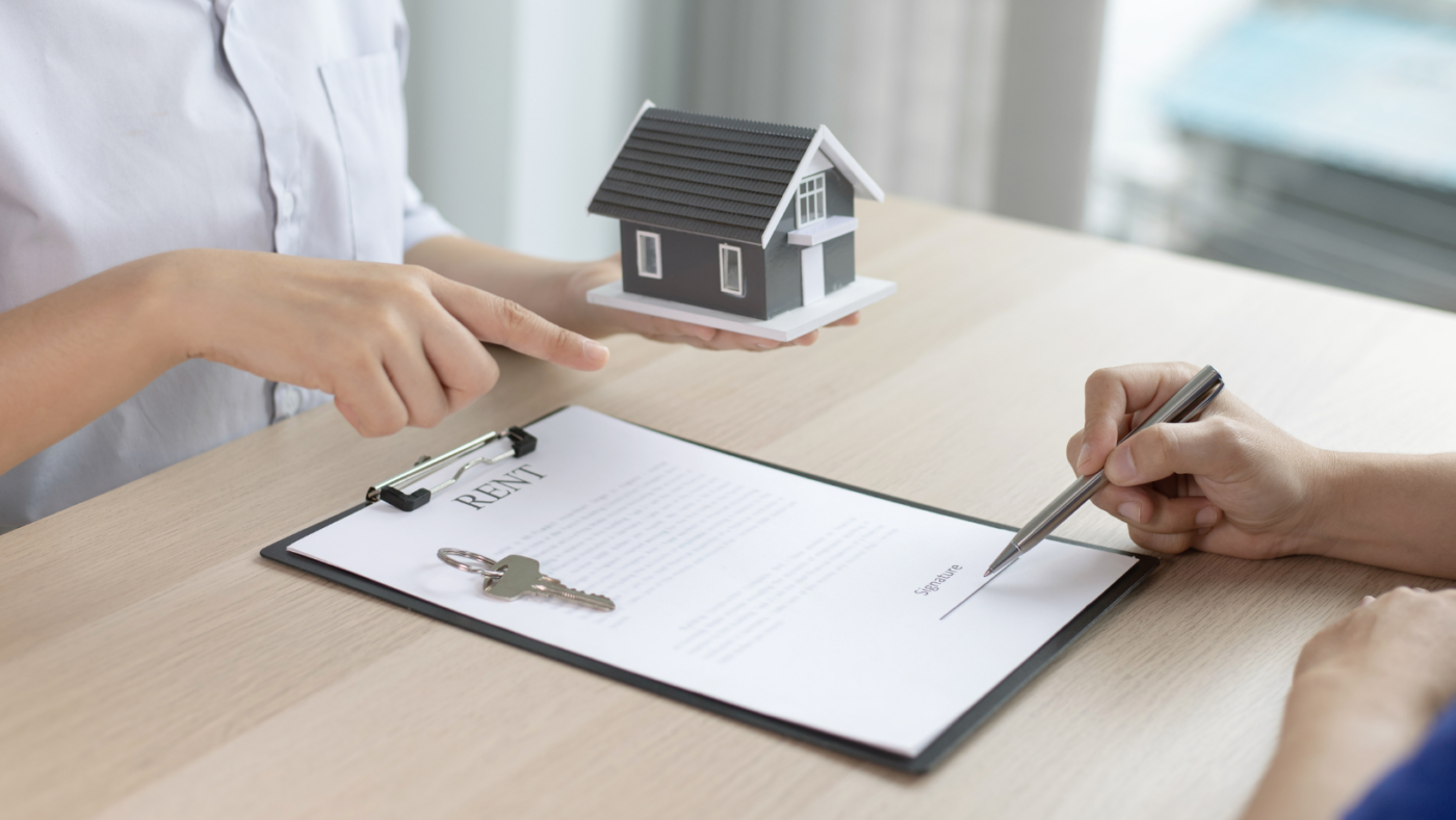 Man with pen signing rental document with a set of keys. 
